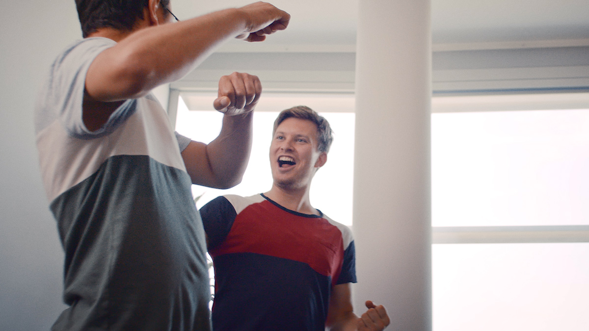 Zwei Kollegen lachen und jubeln beim Tischfußballspiel im Büro. Sie sind locker in T-Shirts gekleidet.