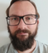 Porträt eines Mannes mit Brille, Vollbart und kurzem Haar vor einem weißen Hintergrund.