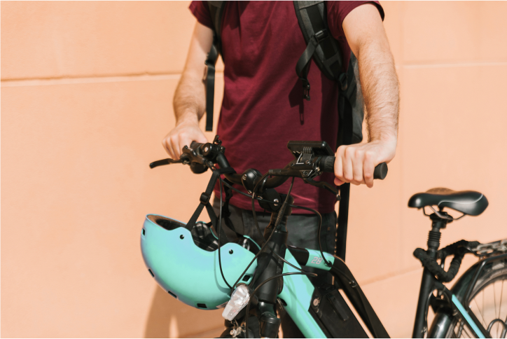 Ein Mann mit Rucksack steht neben einem türkisfarbenen E-Bike und hält den Lenker. Ein passender türkisfarbener Helm hängt am Fahrrad.