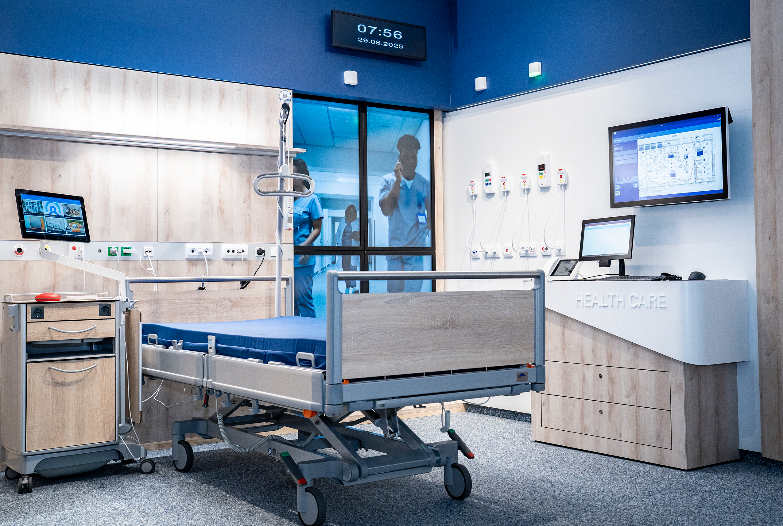 Ein Patientenzimmer in einem Spital. Zu sehen ist ein Krankenbett mit blauer Auflage sowie einige Kästen und Screens.