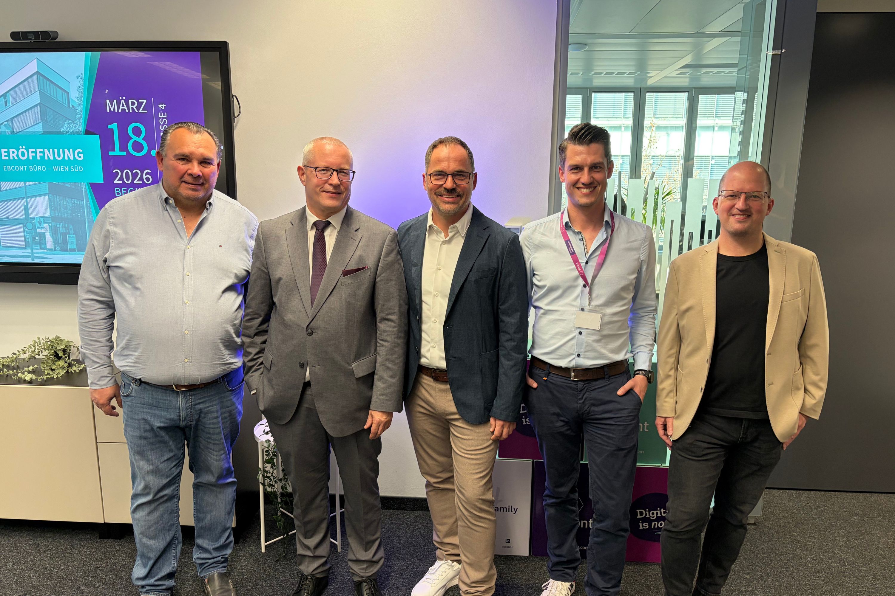 5 men are standing in front of a white wall smiling.